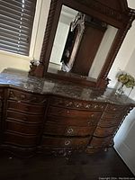Side angle of dark wood dresser with marble top and multiple drawers, showing carved wood details and mirror frame.