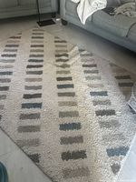 White carpet with rows of rectangular blocks in blue, grey, and beige, laid out beside a grey sofa and floor tiles.