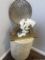 Front view of decorative sculpture set on pedestal featuring white orchid, arch sculpture, round metal wall art