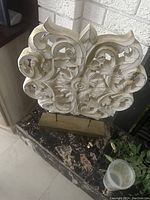 White intricate cut work decorative sculpture mounted on a rectangular base on a marble surface against a brick wall.