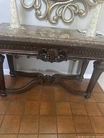 Front view of antique entryway table showing carved wood details and granite top with two decorative vases.