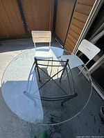 Top view of round glass table with two white chairs placed around it on an outdoor patio.