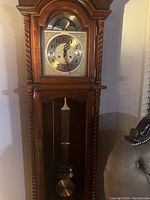 Front upper view showing the ornate wooden case and metallic clock face with black numbers