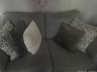Front view of gray two-seater sofa with five cushions visible including two floral patterned, two dark gray, and one cream cushion