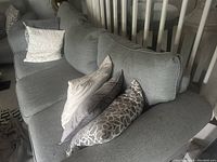 Photo showing gray three-seater sofa with multiple cushions along backrest and armrest, fabric texture visible.