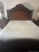 Front view of the king size bed showing detailed carved wooden headboard with floral motifs and chevron wood paneling.