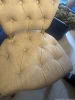 Close-up photo showing the beige button-tufted fabric seat and backrest with natural wood legs of the dining chair.