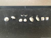 All five pairs of silver earrings arranged in a single row on a black background showing variety in shape and texture.