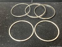 Five silver bangles displayed on a black surface showing variation of texture and size.