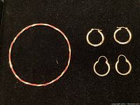 Full overview of the enamelled bracelet and two pairs of gold hoop earrings on black background.