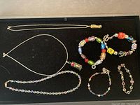 Full view of the 3 necklaces and 4 bracelets arranged on black velvet background showing the silver chains, multicolor glass beads and pendants with detailed colors and shapes.