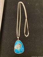 Full view of the silver chain and blue agate geode pendant on black background.