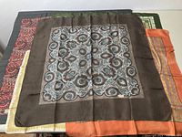 Overview of five vintage silk scarves stacked, showing various patterned and colored borders including brown, orange, green, cream, and red.