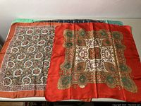 Two Liberty of London silk scarves laid flat showing contrasting patterns and colors, one with burnt orange border and central medallion pattern