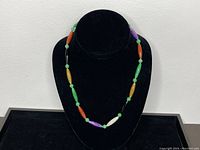 Full view of multicolour jade necklace displayed on black bust.