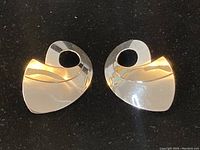 Pair of abstract heart-shaped earrings showing silver and gold tone metal with smooth polished finish on black background.