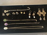 Overview photo showing entire collection of gold filled jewelry including necklaces, earrings, and bracelet arranged on black background