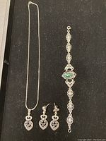 Full view of the necklace with sapphire pendant, matching earrings, and sterling bracelet with green stone on black background.