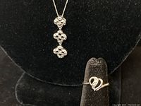 Close-up image of the white gold chain pendant with diamond chips and the white gold swirl ring on display stand.