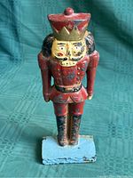 Front-facing view of the antique cast iron nutcracker soldier doorstop standing on a fabric surface with a blue-green checkered pattern.