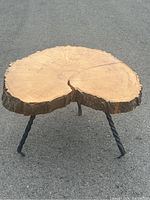 Clear view of the handmade accent table showing the top surface with natural wood rings and bark edges, supported by three twisted steel pin legs.