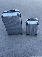 Two silver Swiss Wenger hard-shell suitcases side by side on pavement, showing front and size comparison.