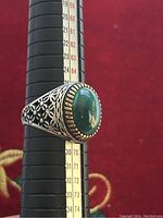 Side view of the silver ring on a measuring mandrel showing size 12 and detailed filigree pattern on band with green stone and decorative bezel.