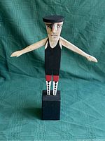 Full view of hand-painted wooden whirligig figure mounted on black block base, showing arms outstretched horizontally.