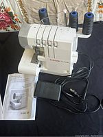 Front view of the SINGER ProFinish 14CG744 serger showing the thread cones, tension dials, and foot pedal along with the instruction manual.