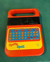 Front view of Texas Instruments Speak and Spell showing keyboard, display, speaker grille, and branding.