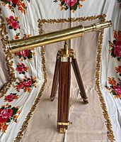 Full view of vintage brass telescope on wooden tripod stand against a floral backdrop