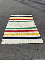 Full view of the Hudson Bay point blanket laid flat outdoors showing horizontal colored stripes and cream background.