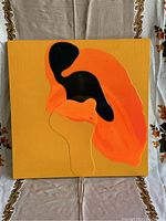Front view of vibrant orange and black abstract oil painting on mustard yellow board, set against patterned fabric.