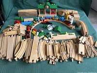 Full layout of wooden train tracks, multiple curved and straight pieces with assembled circular track with trains and accessories around it including station