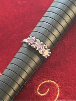 Close-up of the silver ring showing the three purple round stones on a red velvet background, on a ring sizing tool to indicate size 9.