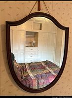 Front view of crest-shaped mirror showing wood frame and full reflective surface in a bedroom setting.
