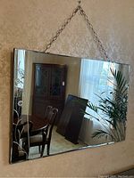 Full view of the rectangular etched glass wall mirror hanging on the wall, showing floral designs on sides and chain.