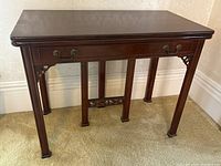 Front view of wooden folding games table showing flat tabletop, drawer front style apron, and square legs.