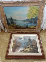 Photo showing two framed landscape paintings: one larger by Skell with ornate frame, one smaller by J.M. Donald with wooden frame.