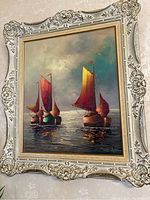 Full view of the framed painting showing three sailing boats with red and yellow sails on water, set in an ornate, decorative carved frame.
