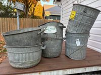 Six galvanized metal bins arranged on an outdoor wooden surface in daylight with fall foliage background