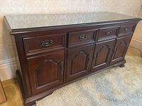 Front view of dark wooden sideboard with glass top showing 4 doors and 4 drawers with brass hardware