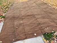 Full spread of the large brown canvas tarp laid out on grass and sidewalk, showing overall size and shape.