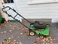 Side view of green LawnBoy Silver Series lawn mower on pavement covered with autumn leaves, showing general structure, wheels, handle and mower deck.
