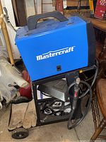 Blue and black Mastercraft MIG welder mounted on wheeled cart, viewed from front and left side