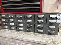 Front view of a gray metal 24 drawer cabinet with labeled drawers containing bolts, screws, electrical hardware, anchors, washers, clamps.