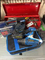 Red metal toolbox open with assorted tools inside including files and manual tools, placed behind the cordless drill set and Tap & Die set box.