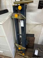 Folded mitre saw stand leaning against a cabinet, showing the yellow adjustment knobs and metal clamps.