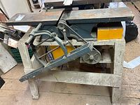 Side view of the wood planer mounted on its metal stand showing the lever mechanism and feed rollers.