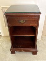Front view of the wooden side table showing the drawer, open shelf, and glass top protector.